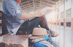 a man sitting on top of a wooden bench next to suitcases and a hat