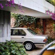 a white car parked in front of a building with purple flowers hanging from it's roof