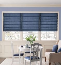 a dining room with blue walls and white furniture in the corner, along with two windows that have roman shades on them