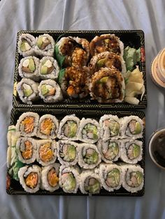 two trays filled with different types of sushi on a bed next to cups and saucers