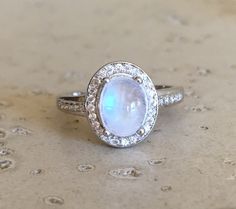 a white ring with a rainbow colored stone surrounded by diamonds on top of a table