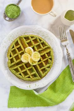 a waffle topped with bananas on top of a white plate next to two cups of coffee