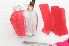 a jar with red paper and scissors next to some cut up pieces of paper on a white surface