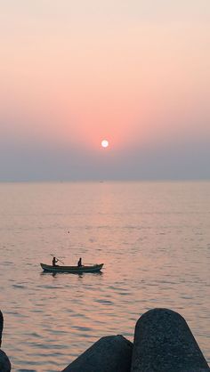 a person in a small boat on the water at sunset or dawn, near rocks