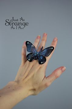 a woman's hand holding a blue butterfly on her finger with the caption just as strange as i am