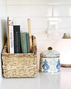 a basket filled with books sitting on top of a kitchen counter next to a lamp