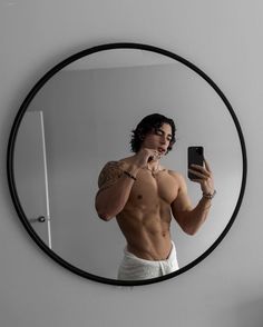 a shirtless man taking a selfie in front of a mirror with his cell phone