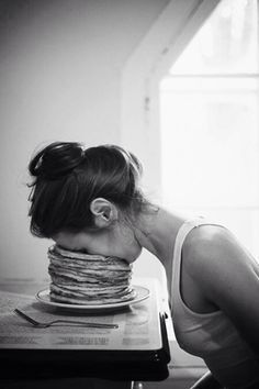 a woman sitting at a table in front of a stack of pancakes on her head