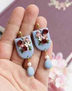 a hand holding two small earrings with flowers on them