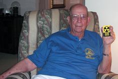 an older man sitting in a chair holding up a yellow and black object with radioactive symbols on it