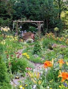 a garden filled with lots of flowers next to a wooden bench on top of a lush green field