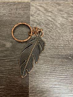 a metal keychain with a leaf on it sitting on top of a wooden table