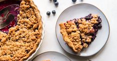 blueberry crumble pie on two plates next to a fork and bowl of berries