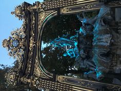 an ornate mirror reflecting the sky and trees