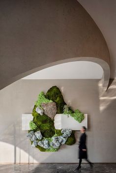 a man walking past a sculpture made out of moss and rocks on the wall in an office building