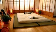 a bed sitting on top of a wooden floor next to a potted plant in front of a window