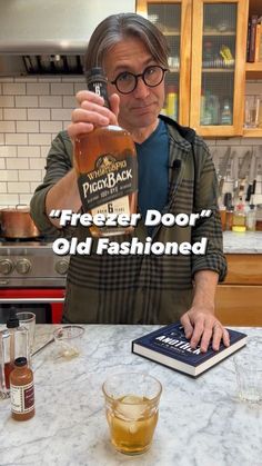 a man holding a bottle of alcohol in his hand while standing at a kitchen counter