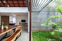 a wooden table sitting under a roof next to a lush green field with lots of plants