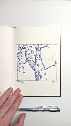 a hand is holding an open book with a drawing of a tree in the middle