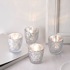 three silver votives sitting on top of a table next to an open book