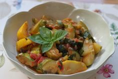 a white bowl filled with cooked vegetables on top of a floral tablecloth covered table