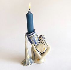 a ceramic candle holder with a blue candle in the shape of a hand holding a vase