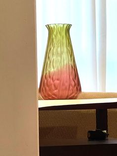 a pink and green vase sitting on top of a wooden table next to a window