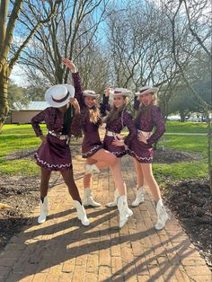 three girls in purple outfits and white hats posing for the camera on a brick walkway