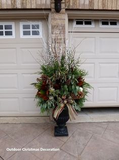 a vase filled with flowers and greenery sitting in front of a garage door next to a lamp post