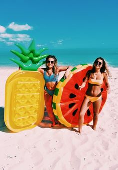 two women in swimsuits on the beach with watermelon and pineapple float