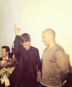 two men are standing next to each other and one is holding flowers in his hand