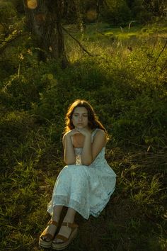 a woman sitting in the grass with her hands under her chin and looking at the camera