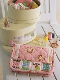 three white boxes with pink quilts and sewing supplies in them on top of a wooden table