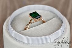 a ring with a green stone in it on top of a white velvet box,