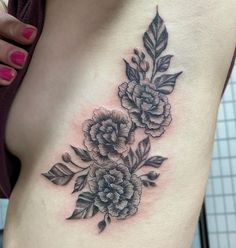 a woman's stomach with flowers and leaves tattooed on her side ribcage