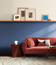 a red couch sitting in front of a blue wall with pictures on top of it