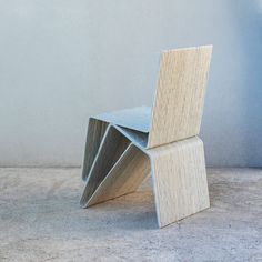 a wooden chair sitting on top of a floor next to a white wall and cement floor