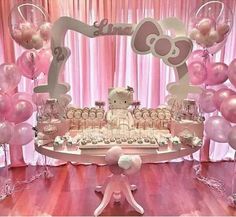 a table topped with lots of pink and white balloons next to a hello kitty cake