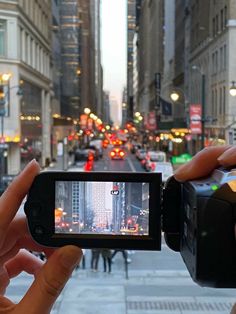 someone holding up a camera in the middle of a city street with buildings and cars