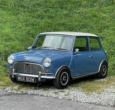 an old blue car is parked on the side of the road in front of some grass