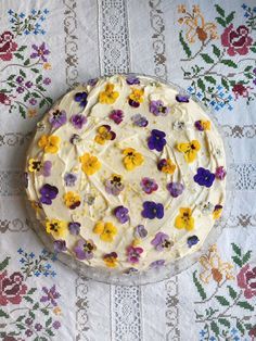 a cake with white frosting and colorful flowers on it sitting on a tablecloth