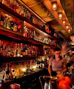 two men are behind the bar with many bottles and glasses on shelves in front of them