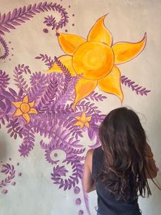 a woman painting a mural on the wall with purple and yellow flowers in front of her