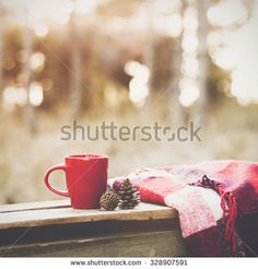 a red coffee cup sitting on top of a wooden table next to a pine cone