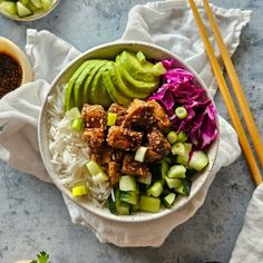 a bowl filled with rice, cucumber and meat next to chopsticks