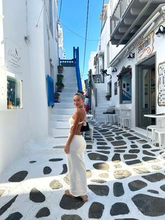 a woman in a white dress is standing on the street and looking at the camera