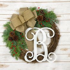 the monogrammed wreath has been decorated with pine cones, berries and a bow