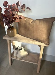 a wooden bench with a vase and plant on it next to a pair of shoes