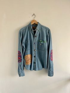 a blue jean shirt with patches on it hanging from a hanger against a white wall