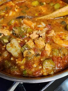 a pot filled with chicken and vegetables on top of a stovetop oven next to a wooden spoon